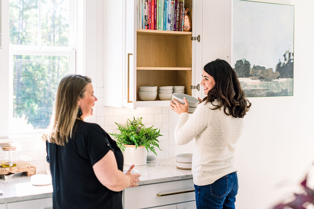 Professional organizer from Clearly Organized NC helping a client organize kitchen cabinets with stacked white bowls in a Clayton, NC home.